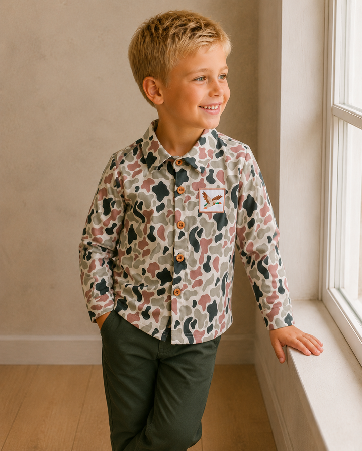 Young boy wearing a patterned shirt standing by a window