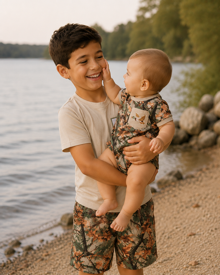 Older boy is holding baby boy by the lake