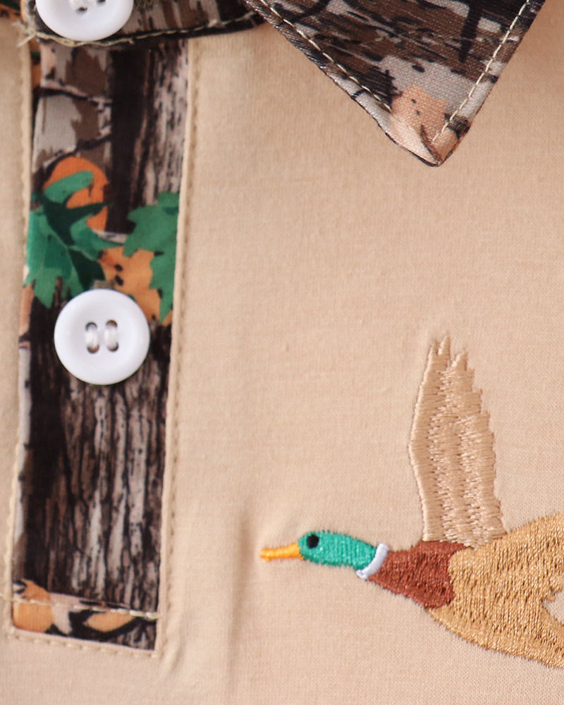 Close-up of a beige fabric with a duck embroidery and camouflage patterned trim.