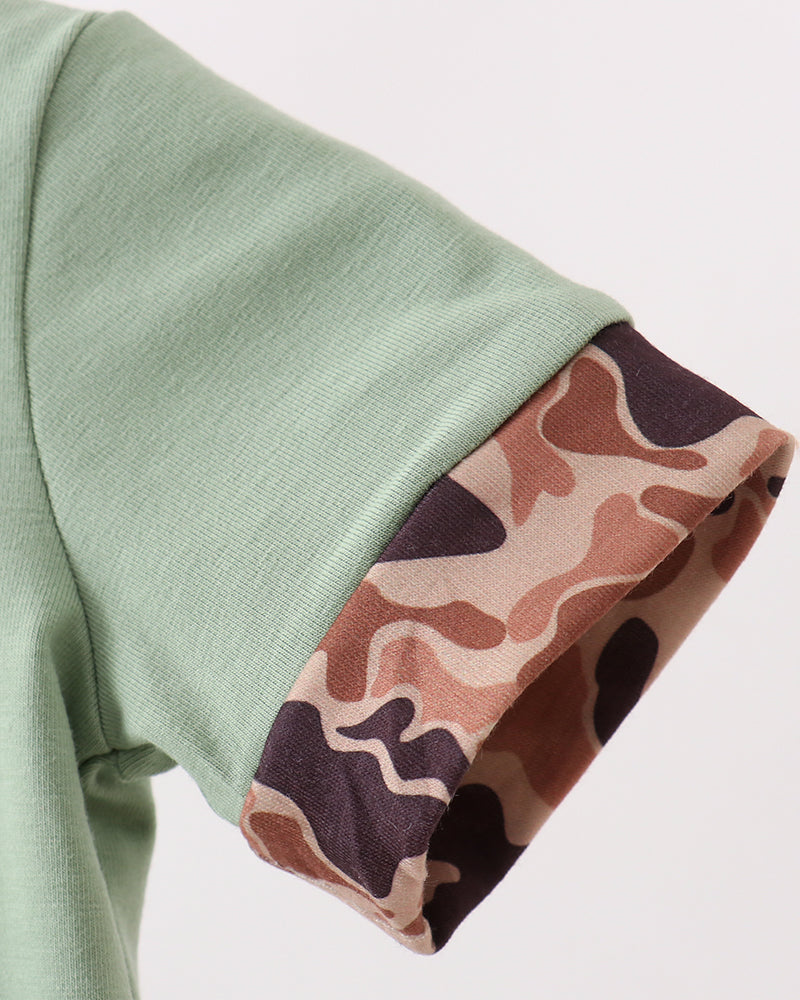 Close-up of a green garment with a camouflage-patterned cuff on a light gray background