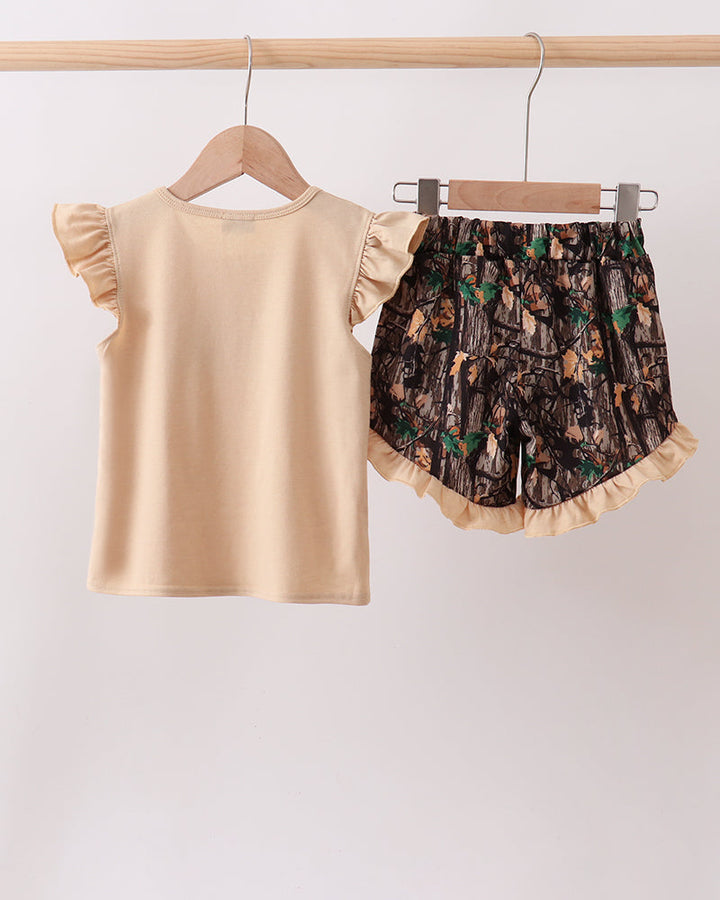 Beige top and patterned shorts hanging on a wooden rod against a white background