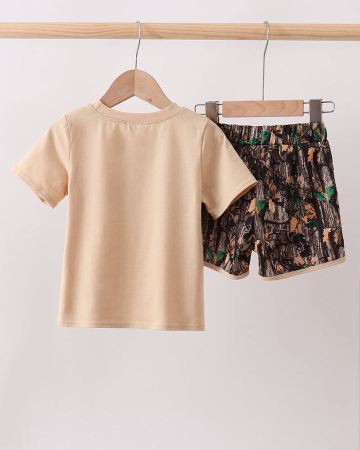 Beige t-shirt and patterned shorts hanging on wooden hangers against a white background