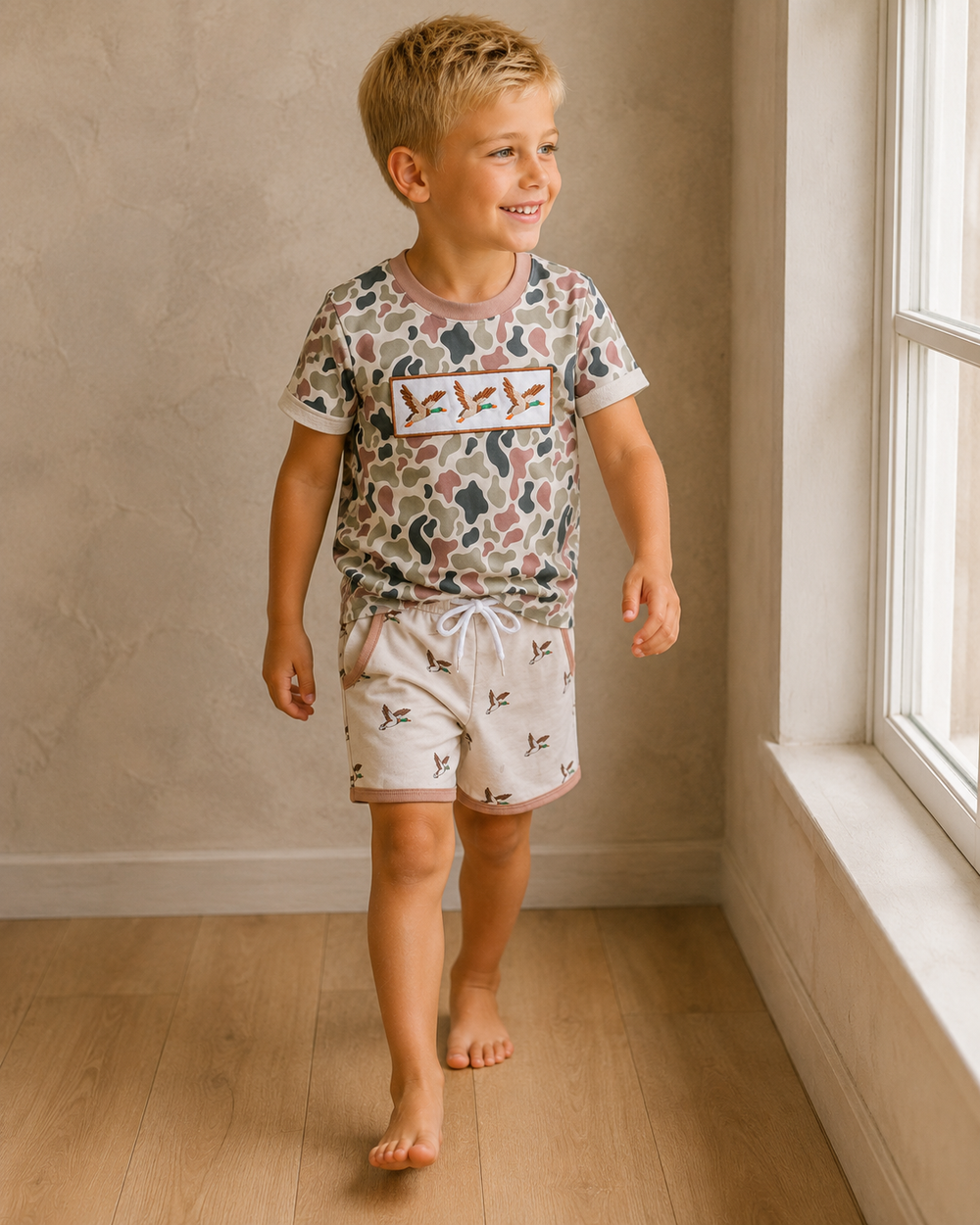 Child wearing a patterned shirt and shorts standing in a room with a window.