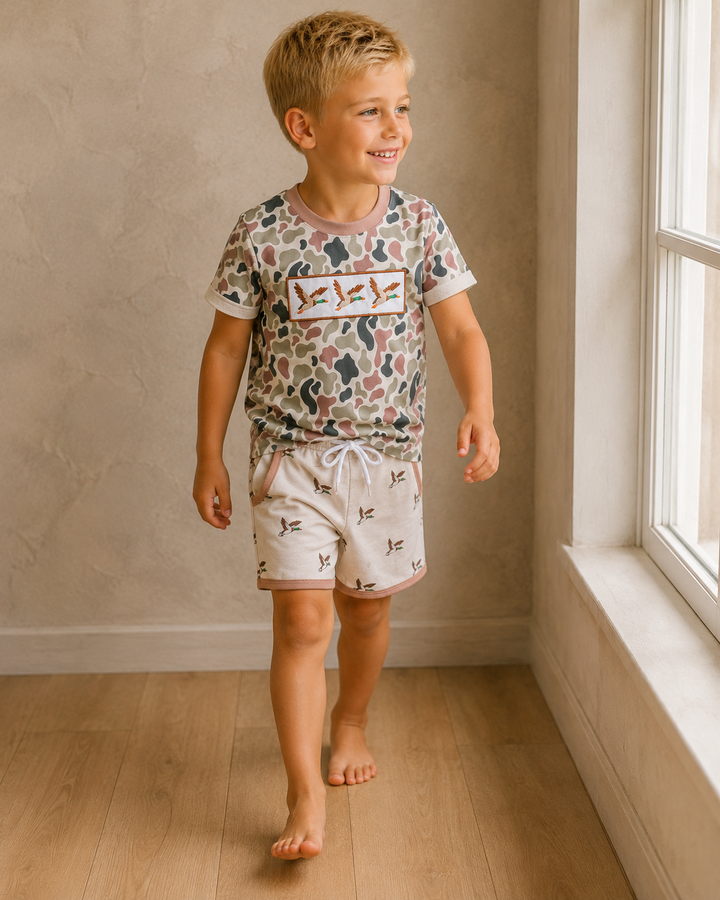 Child wearing a patterned shirt and shorts standing in a room with a window.