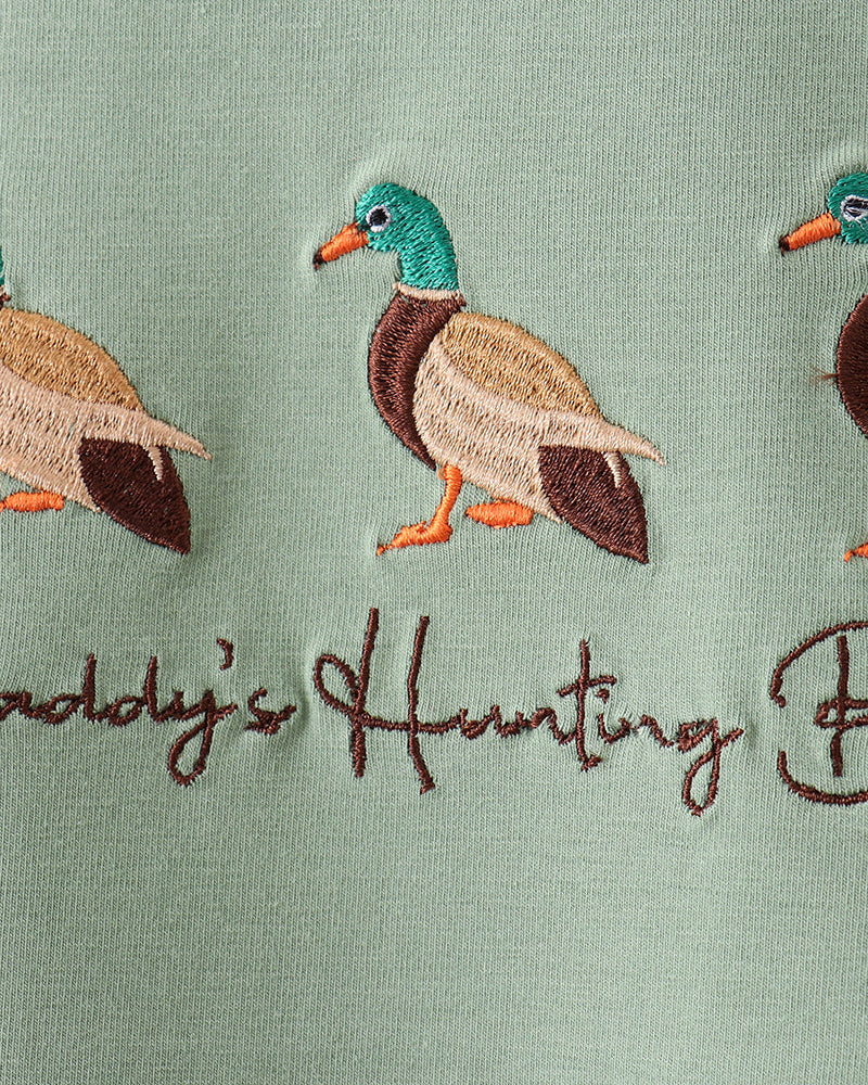Embroidered ducks and text on a green fabric background