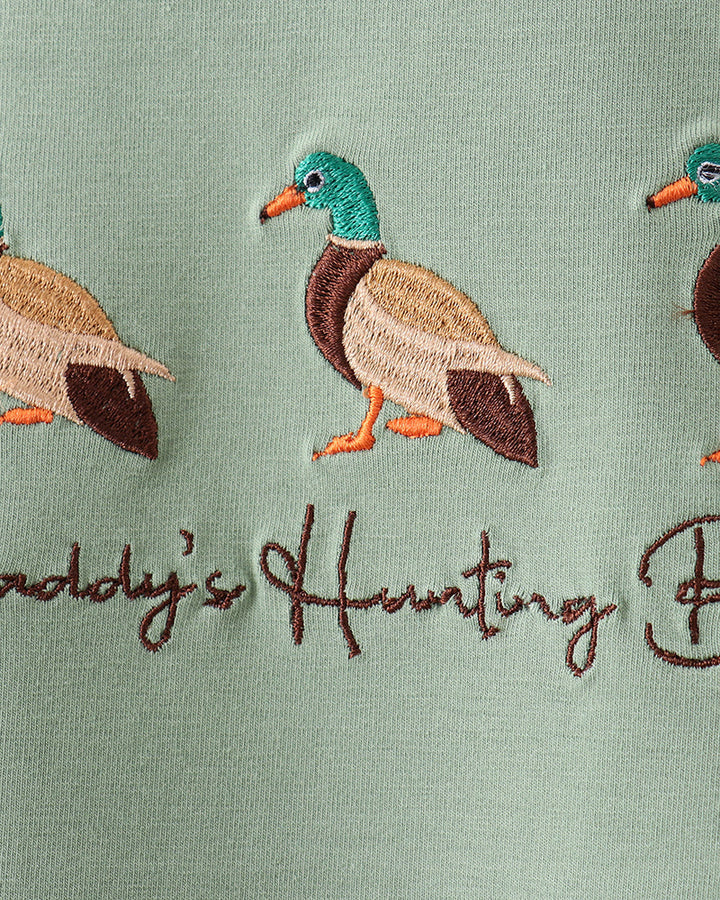 Embroidered ducks and text on a green fabric background