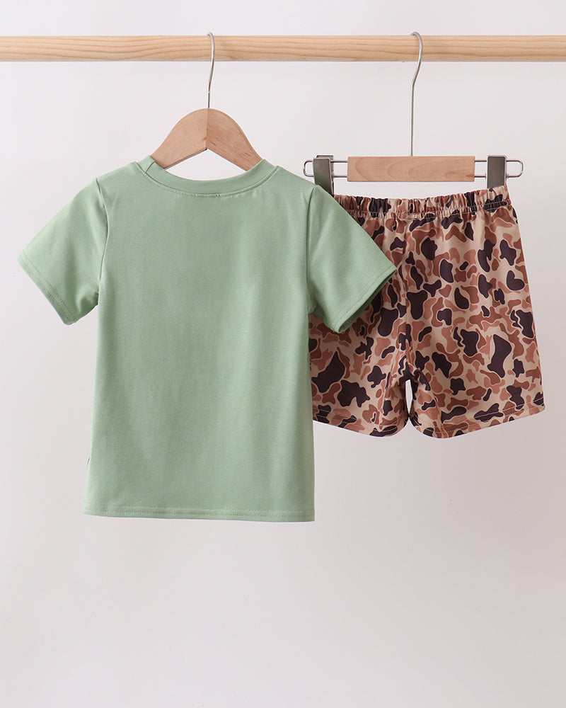 Green t-shirt and patterned shorts hanging on a rack against a white background