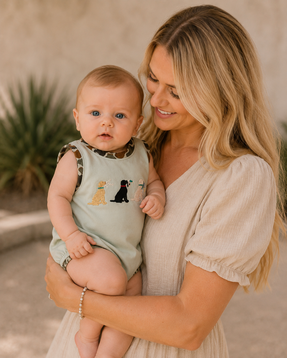 Woman holding a baby wearing a romper with dog illustrations outdoors.