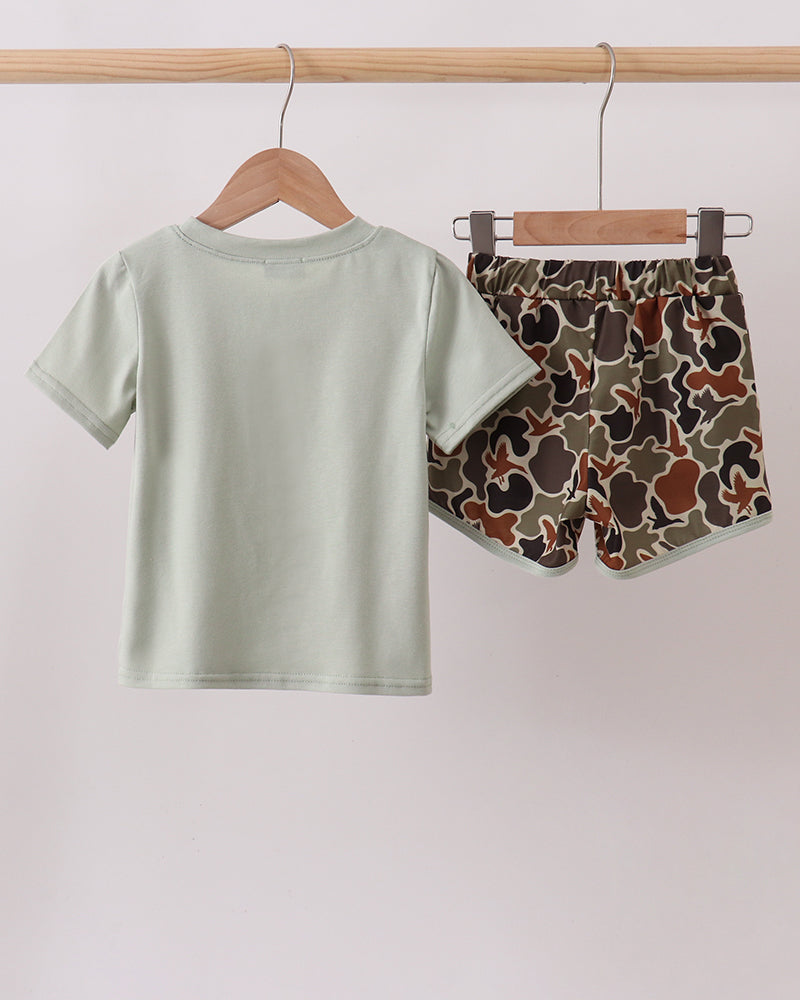 Light green t-shirt and camouflage shorts hanging on a wooden rod against a white background