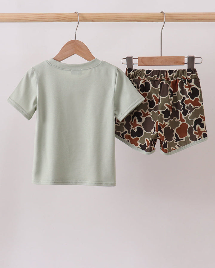 Light green t-shirt and camouflage shorts hanging on a wooden rod against a white background