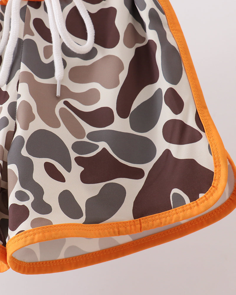 Close-up of a camouflage-patterned drawstring bag with orange trim on a light gray background