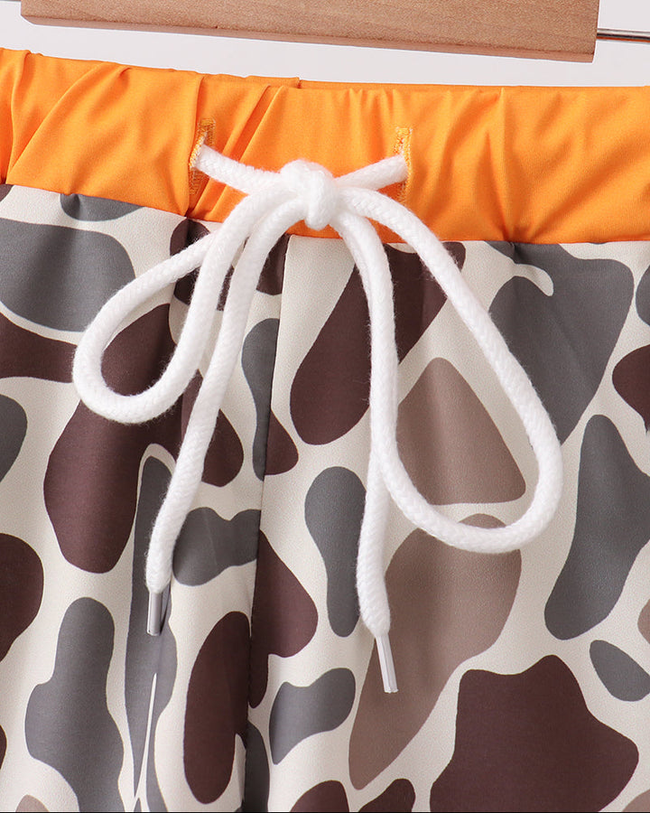 Swim trunks with orange top and brown and beige patterned bottom on a wooden rod.