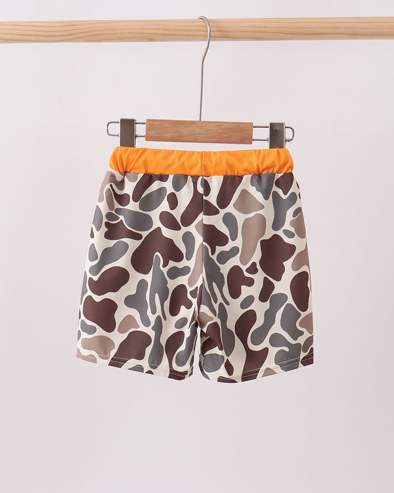 Camouflage-patterned shorts with orange waistband on a hanger against a white background