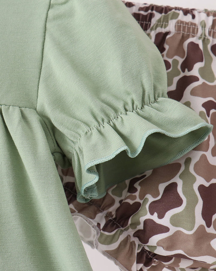 A close-up of a light sage green ruffled sleeve or dress section layered over a brown, beige, and green camouflage patterned garment.