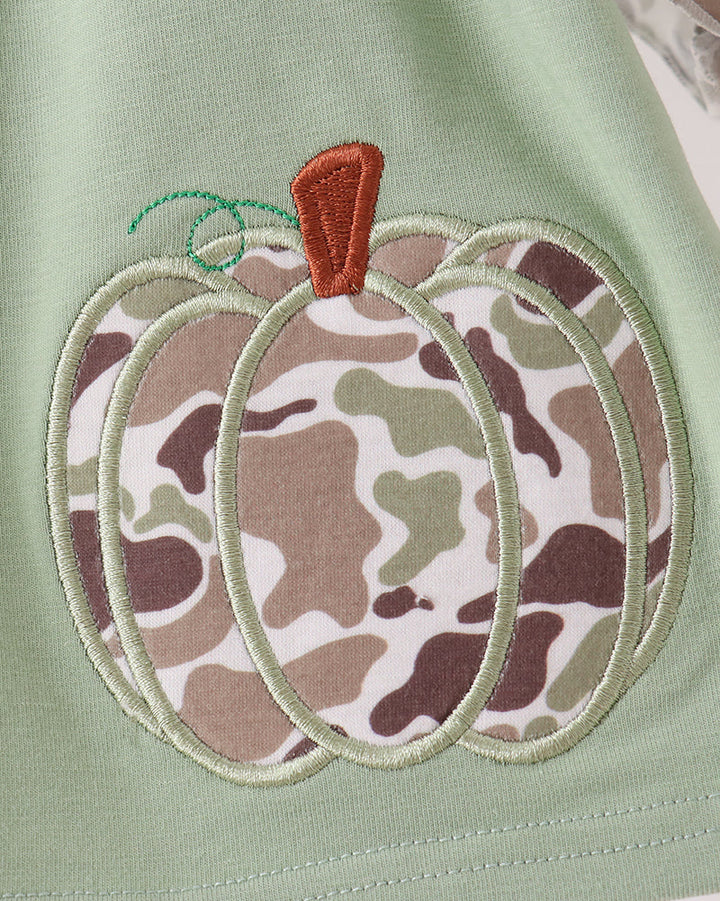 Close-up of a light sage green garment featuring an embroidered pumpkin applique with a camouflage pattern and a small orange stem.