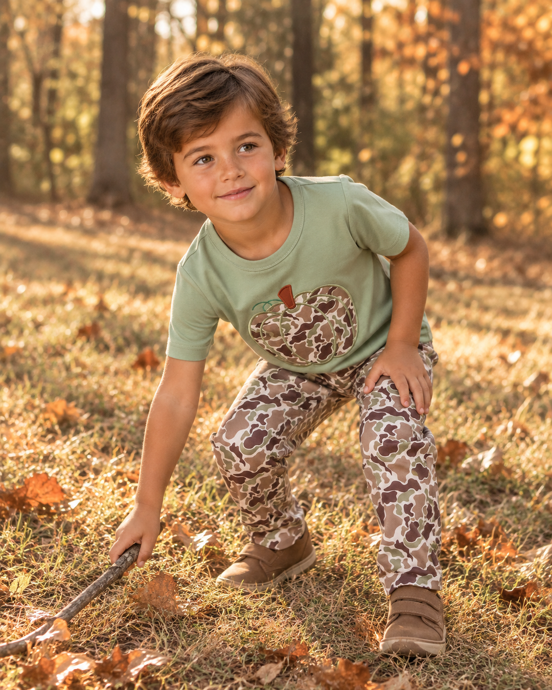 Older boy in camo outfit is picking up a stick.