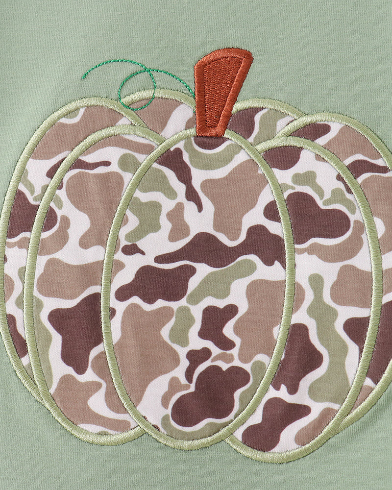 A close-up of a pumpkin-shaped applique or embroidery design on a sage green fabric background. The pumpkin has a camouflage pattern in shades of brown, beige, and olive green, with a small orange-brown stem and a light green stem.