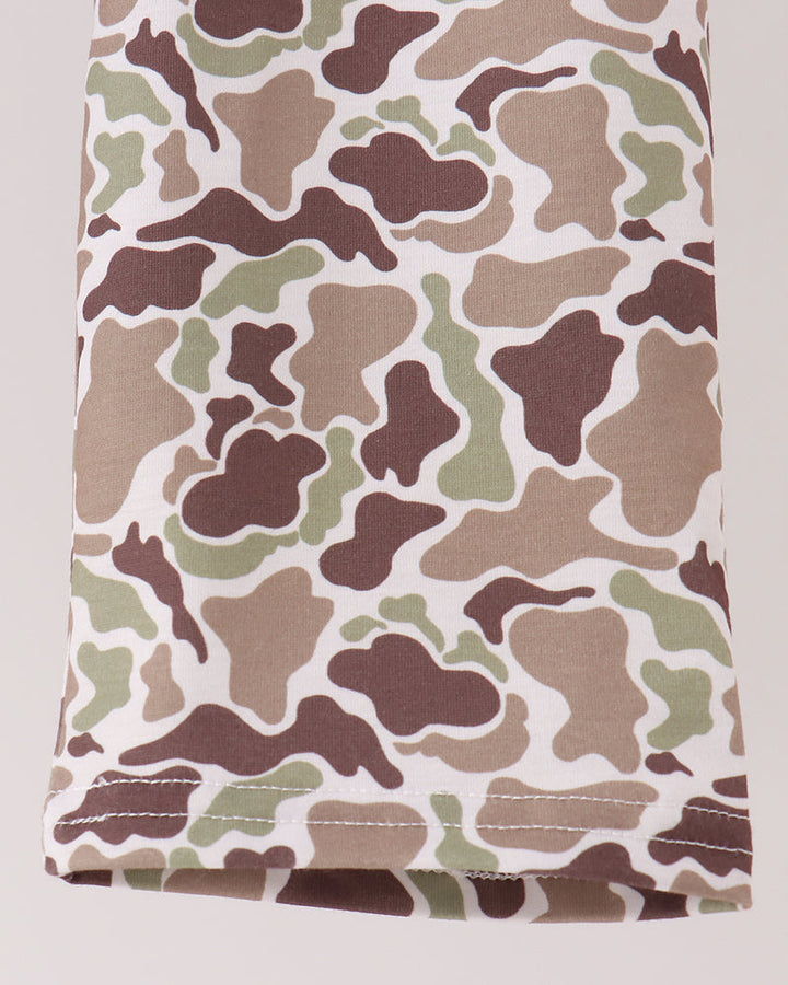 A close-up of a folded garment featuring a classic camouflage pattern in brown, beige, and green on a white base, with visible stitching along the hem.