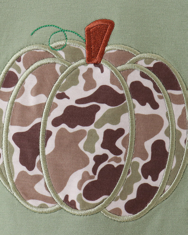 Close-up of a pumpkin applique or embroidery on a sage green fabric, featuring a brown, beige, and olive green camouflage pattern with a small orange-brown stem.