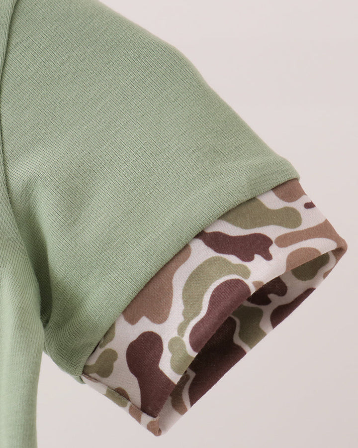 Close-up of a sage green knit garment sleeve with a rolled cuff revealing a camouflage-patterned lining in brown, beige, and olive green.