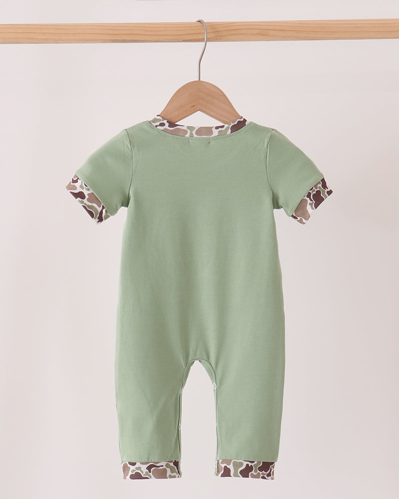 A baby short-sleeve romper in sage green, hanging on a wooden hanger from a light wood bar. The romper features giraffe-print patterned trim along the collar, sleeve cuffs, and leg hems.