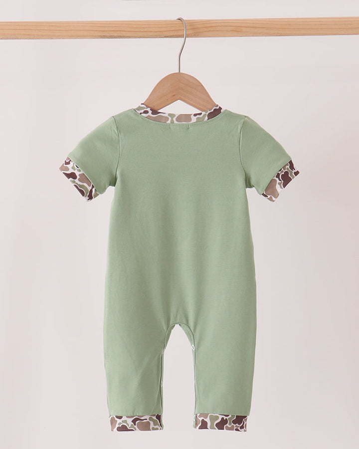 A baby short-sleeve romper in sage green, hanging on a wooden hanger from a light wood bar. The romper features giraffe-print patterned trim along the collar, sleeve cuffs, and leg hems.