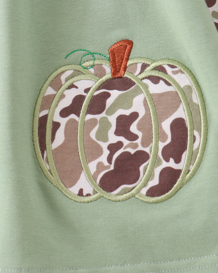 Close-up of a light sage green fabric garment featuring an embroidered pumpkin applique with a brown, beige, and white camouflage pattern body, a light green stitched outline, and an orange stem.