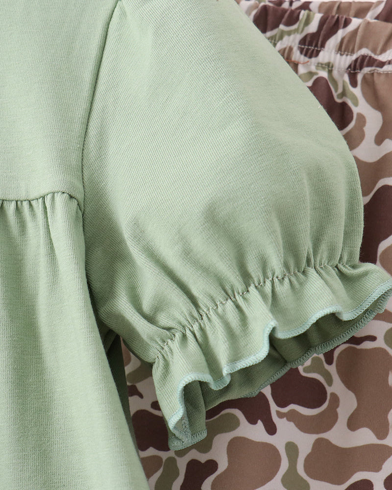 Close-up of a light sage green blouse with a ruffled elbow-length puff sleeve, shown next to a brown and beige camouflage patterned garment.