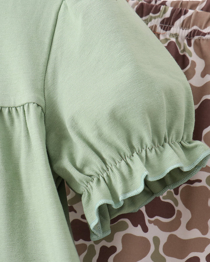 Close-up of a light sage green blouse with a ruffled elbow-length puff sleeve, shown next to a brown and beige camouflage patterned garment.