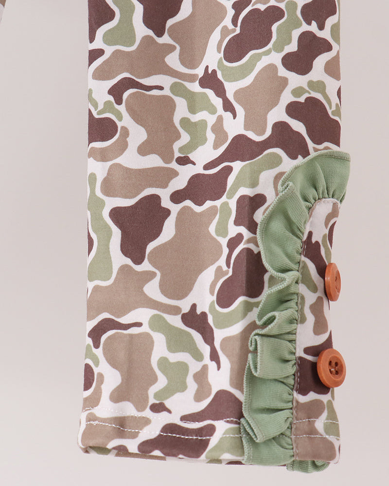 Close-up of a camouflage-patterned fabric sleeve or cuff with a sage green ruffled trim and two brown buttons, shown against a light neutral background.