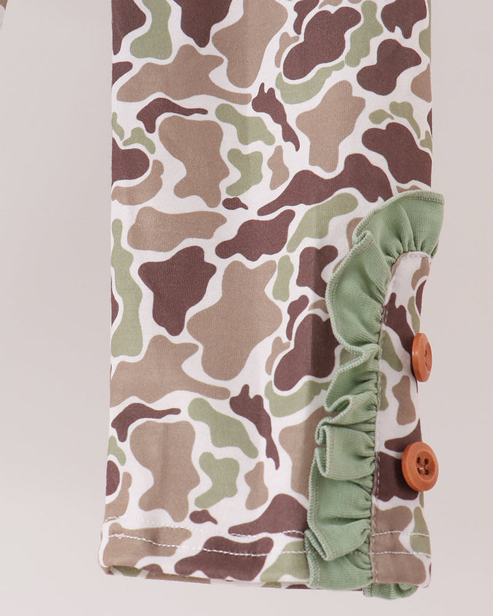 Close-up of a camouflage-patterned fabric sleeve or cuff with a sage green ruffled trim and two brown buttons, shown against a light neutral background.