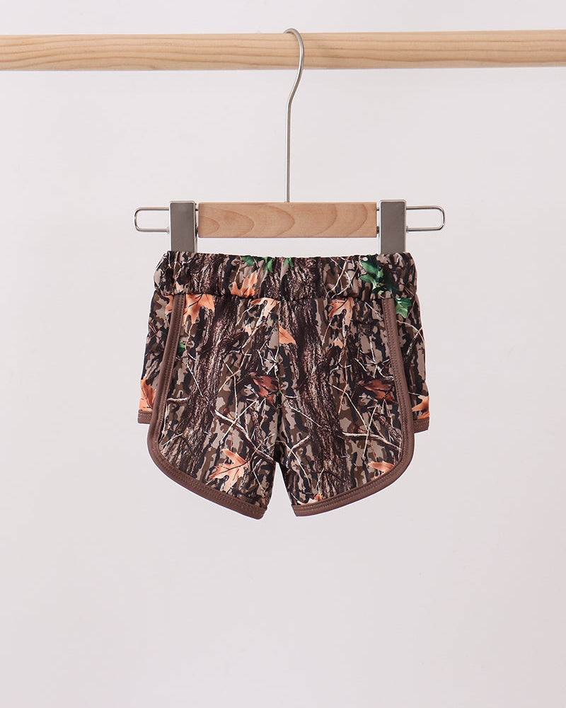 Camouflage-patterned shorts hanging on a wooden hanger against a white background