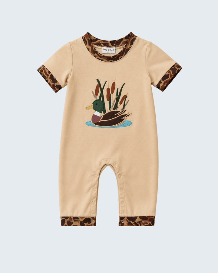 A baby short-sleeve romper in beige with brown and black leopard print trim on the collar, cuffs, and hem, featuring a duck and reeds graphic on the chest.