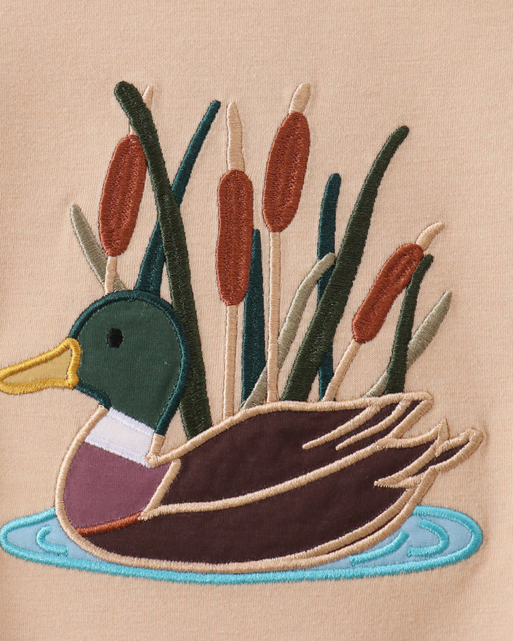 Duck applique graphic on beige romper with colorful reeds and water, close-up