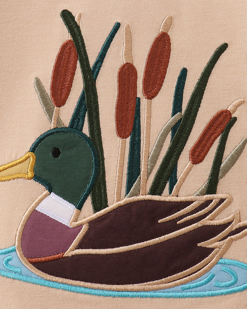 Beige duck applique detail with colorful beak, reeds, and pond border