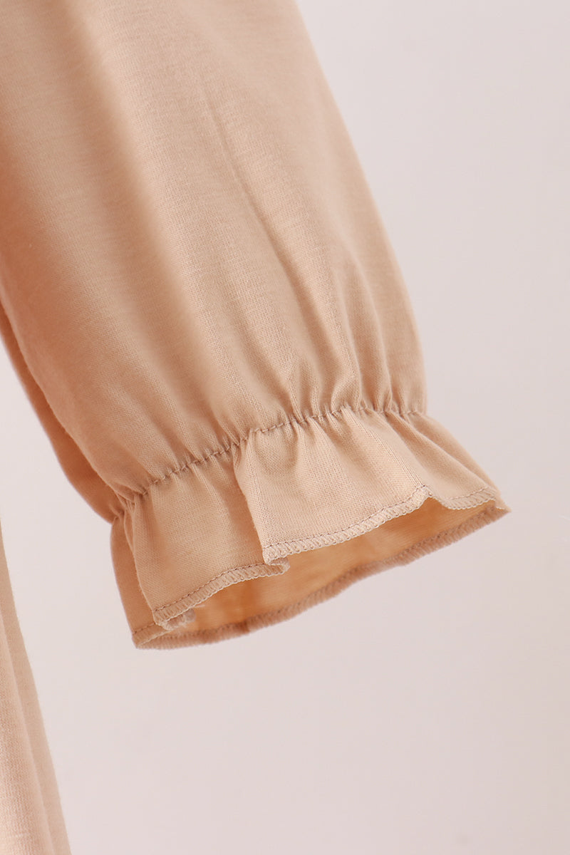Close-up of a beige or light tan fabric garment sleeve with gathered elastic cuffs and a ruffled hem, shown against a plain light background.