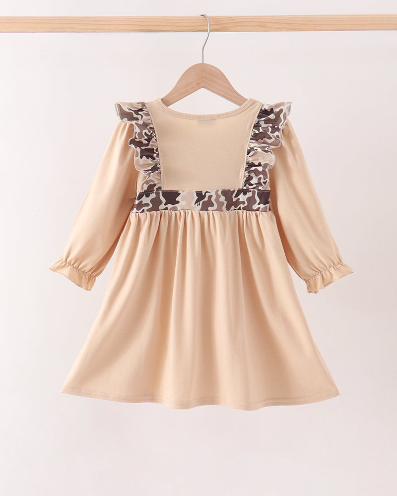 A beige long-sleeve dress with brown and beige patterned ruffle trim on the shoulders, hanging on a wooden hanger against a plain light background.