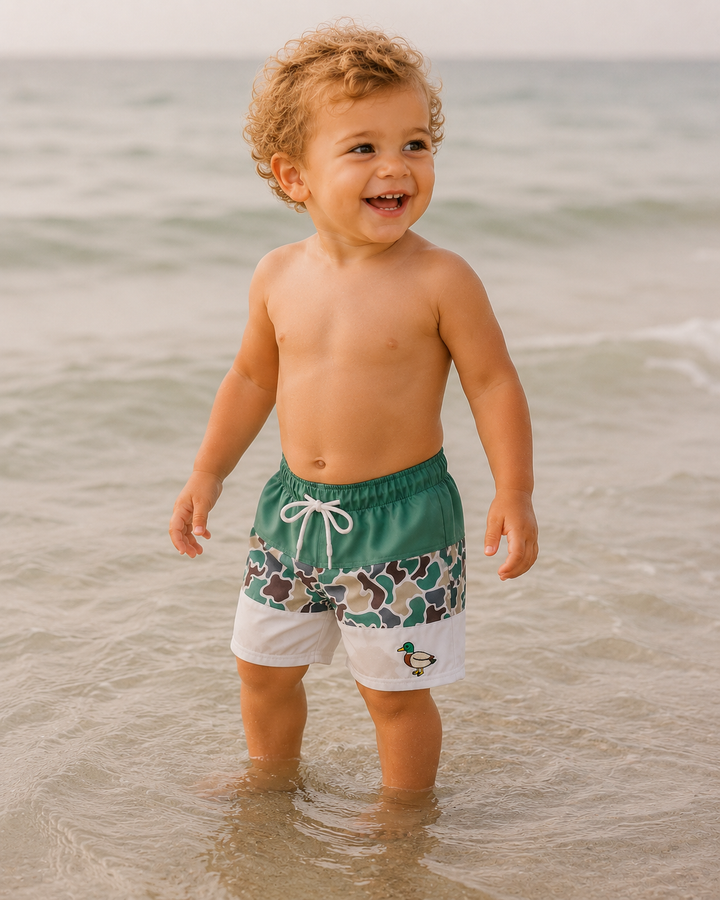 Child wearing green swim trunks with a duck design at the beach