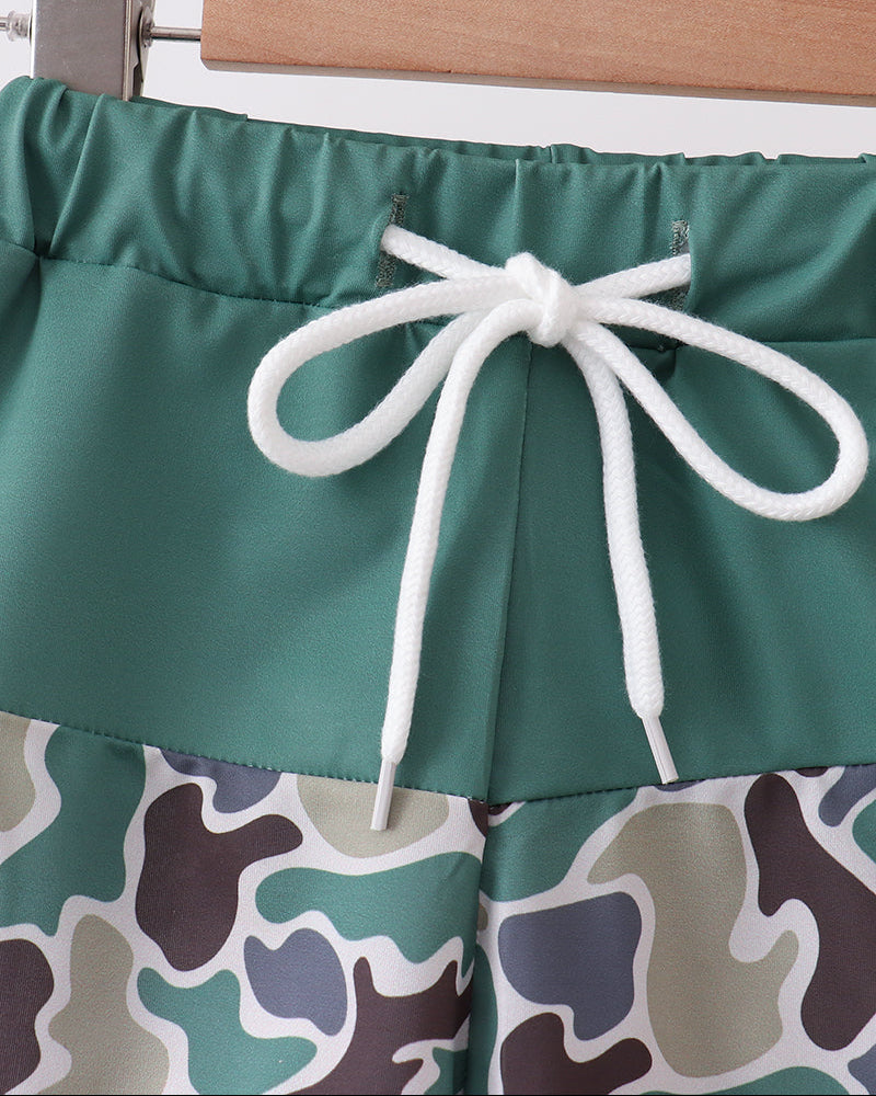 Green shorts with a camouflage pattern and white drawstring on a hanger.