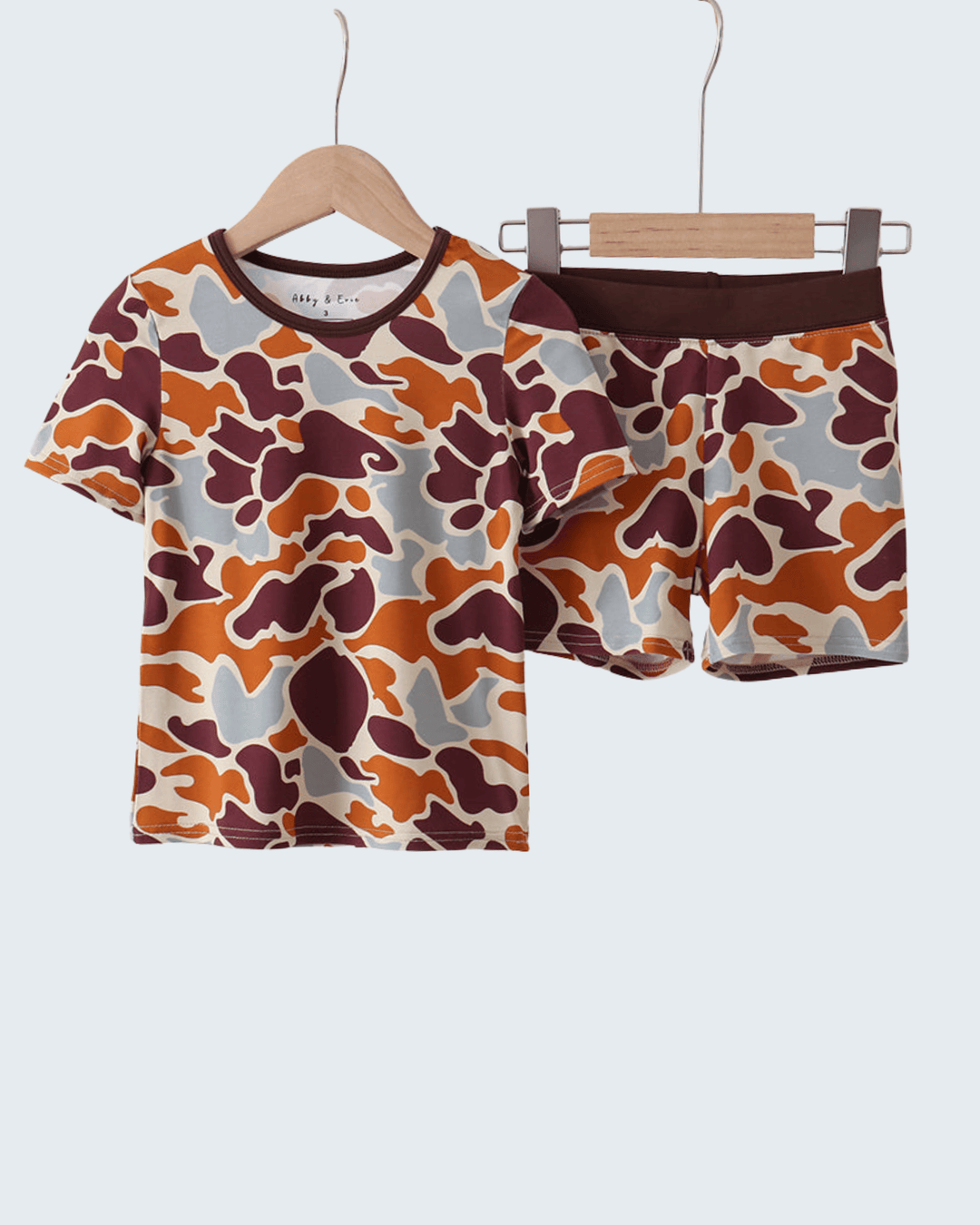 Camouflage-patterned shirt and shorts set on hangers against a white background