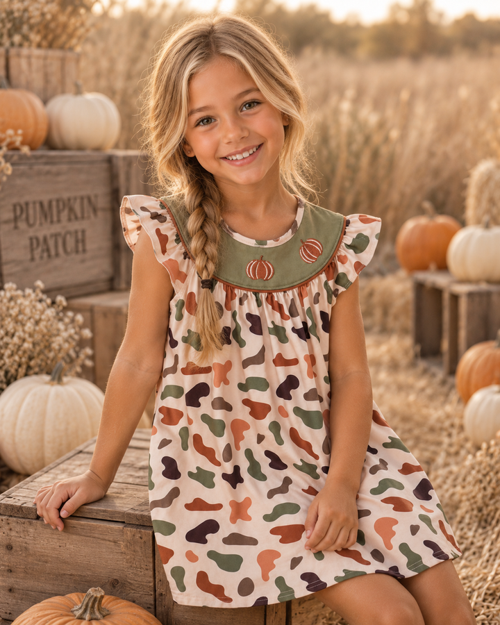 Young girl in a camo dress sitting by pumpkins