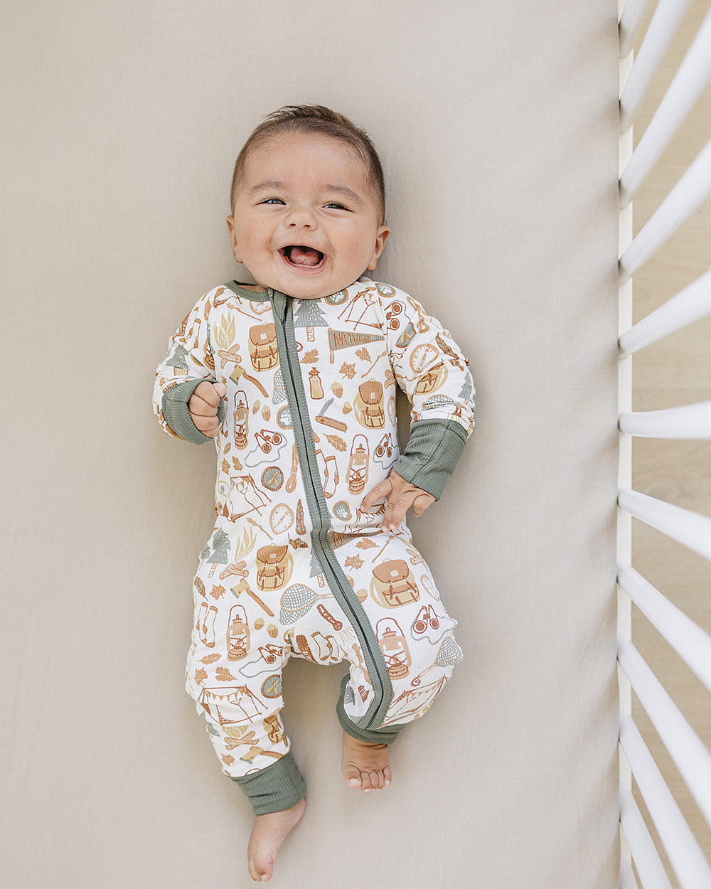 Baby wearing a patterned onesie standing against a neutral wall.