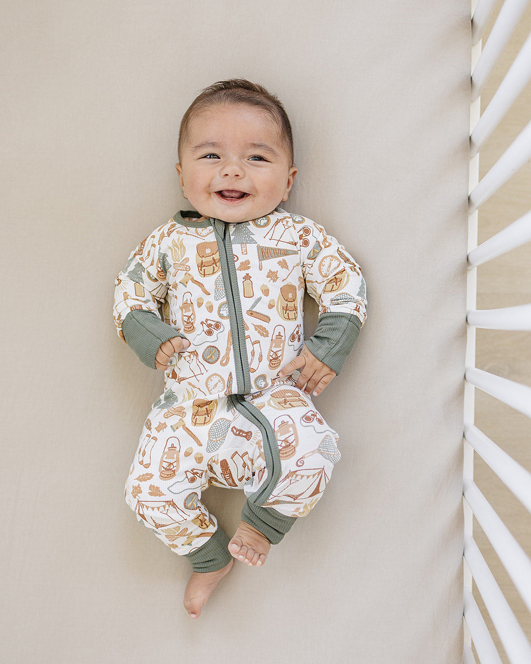 Baby wearing a patterned onesie standing against a neutral wall.