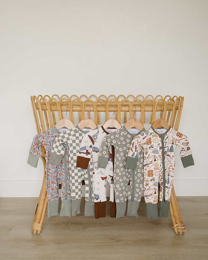 Collection of baby rompers on a wooden rack against a plain wall.