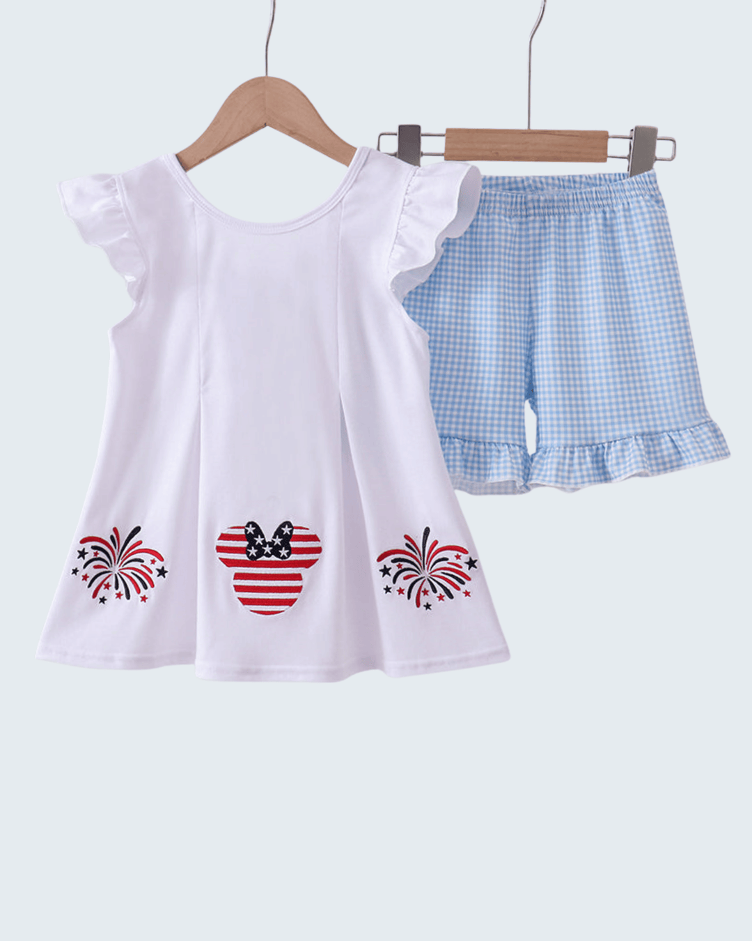 White top with red and blue designs and blue checkered shorts on a hanger against a white background