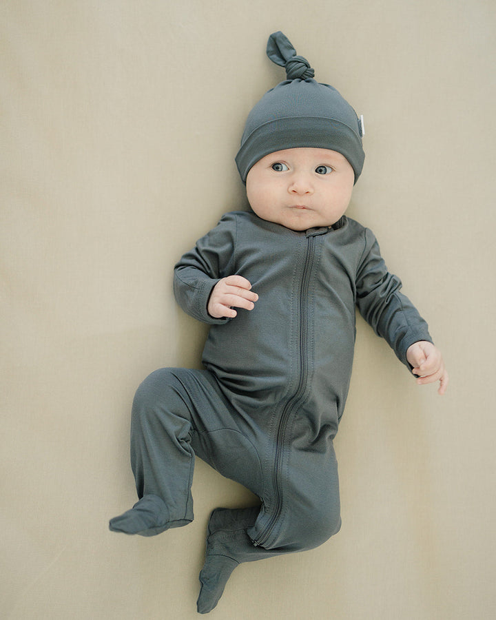 Baby in a gray outfit and hat lying on a beige surface