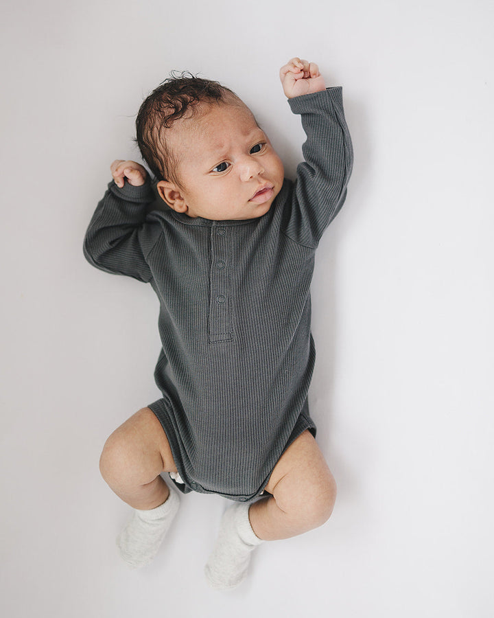 Baby wearing a gray long-sleeve onesie on a white background