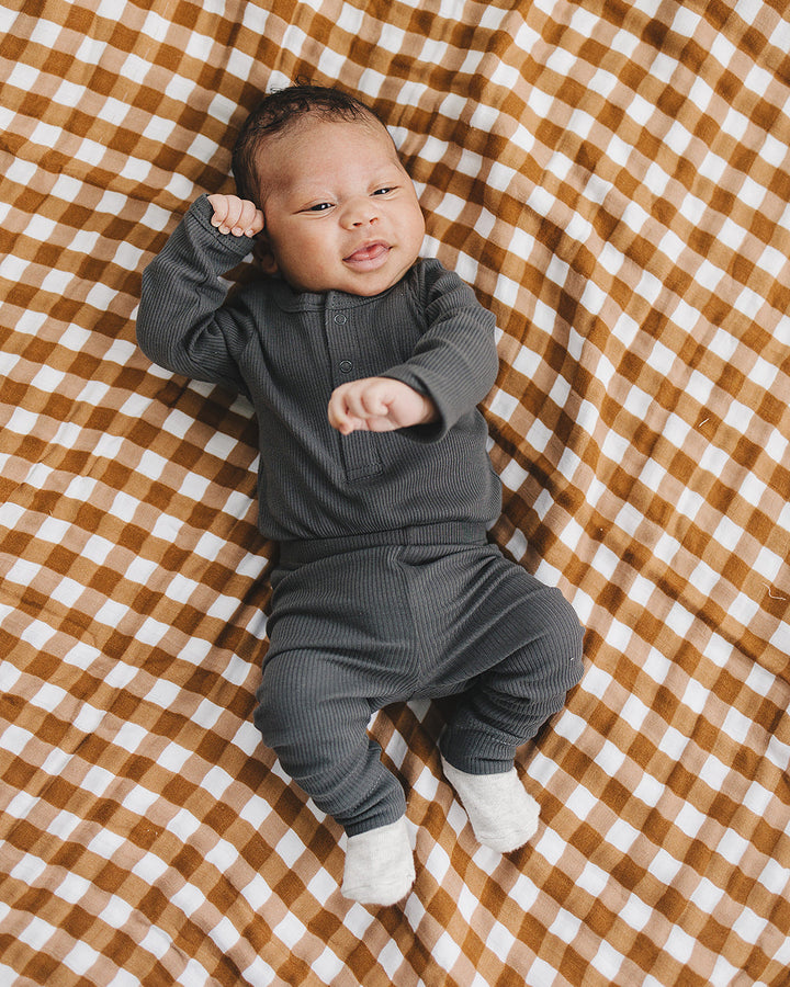Baby in a gray outfit lying on a brown and white checkered blanket