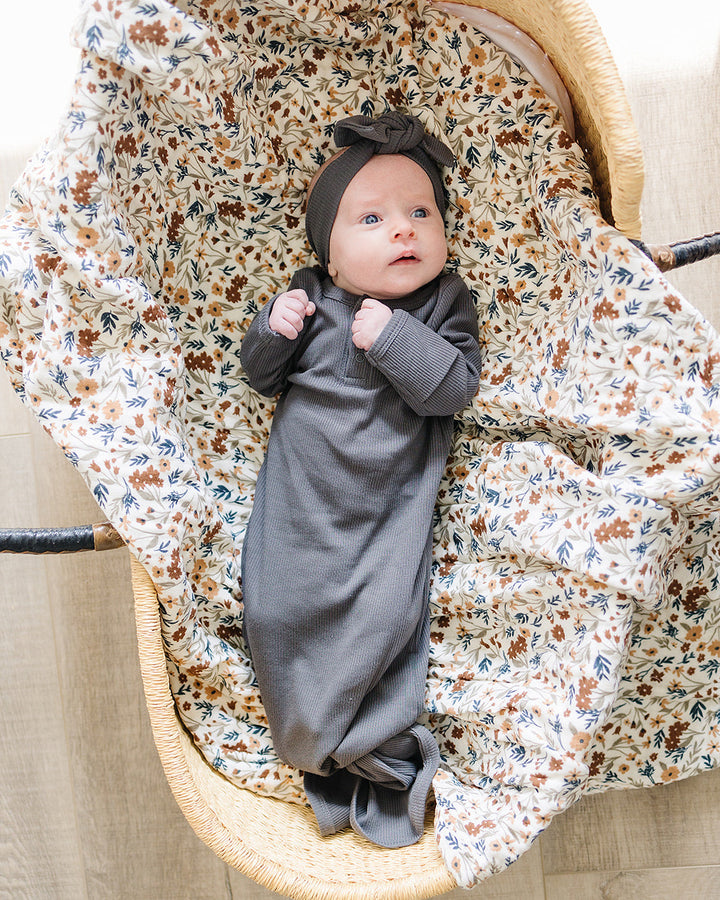 Baby in a gray outfit and floral blanket in a wooden crib