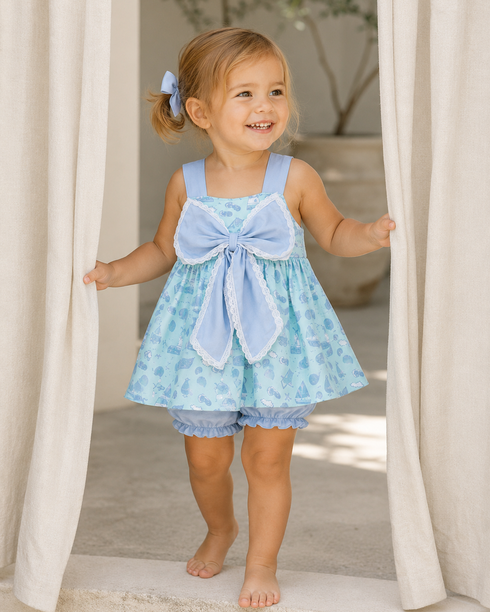 Child wearing a light blue floral dress with a bow standing between white curtains.